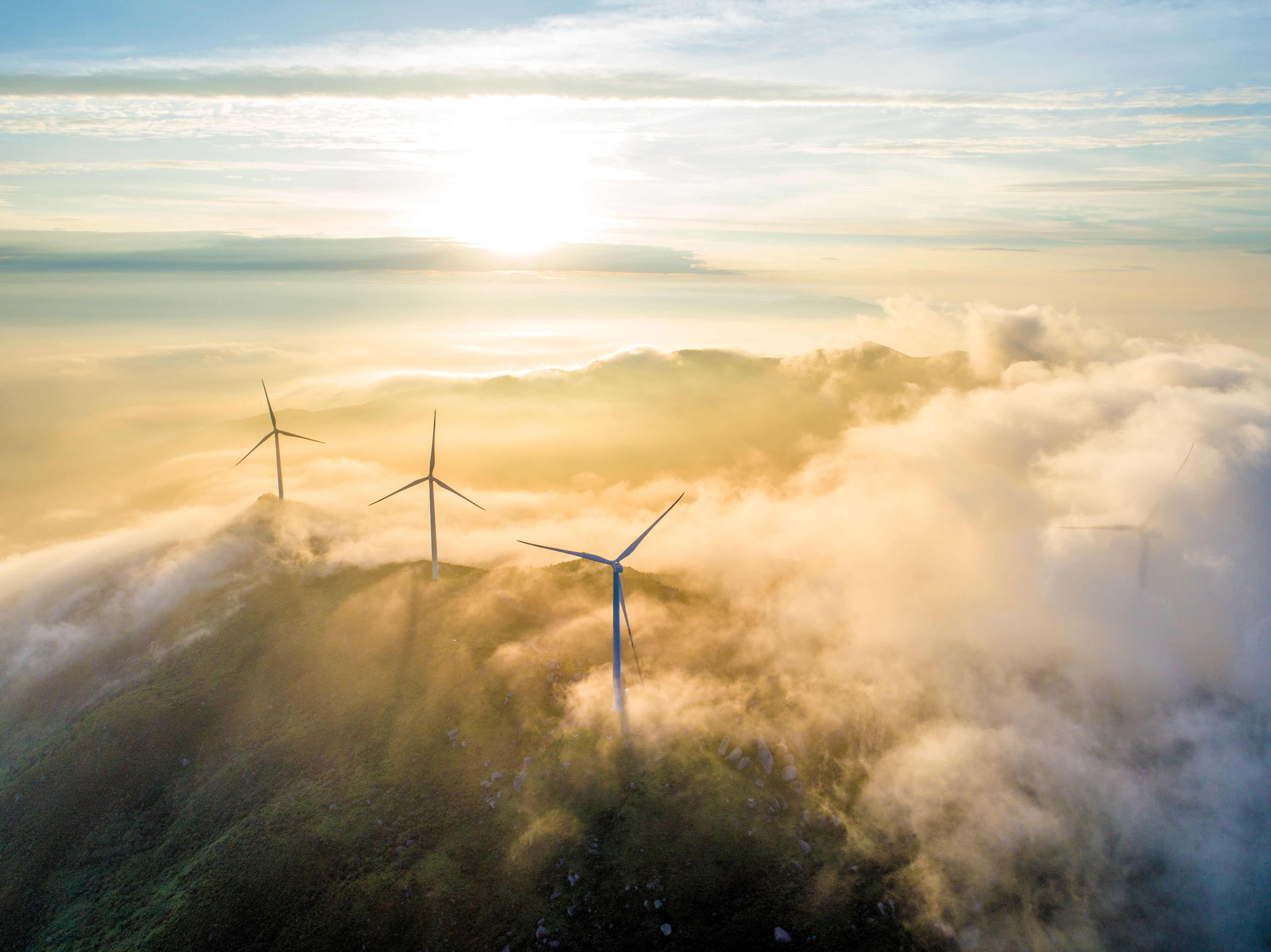 A soaring shot of wind turbines bathed in clouds at sunrise