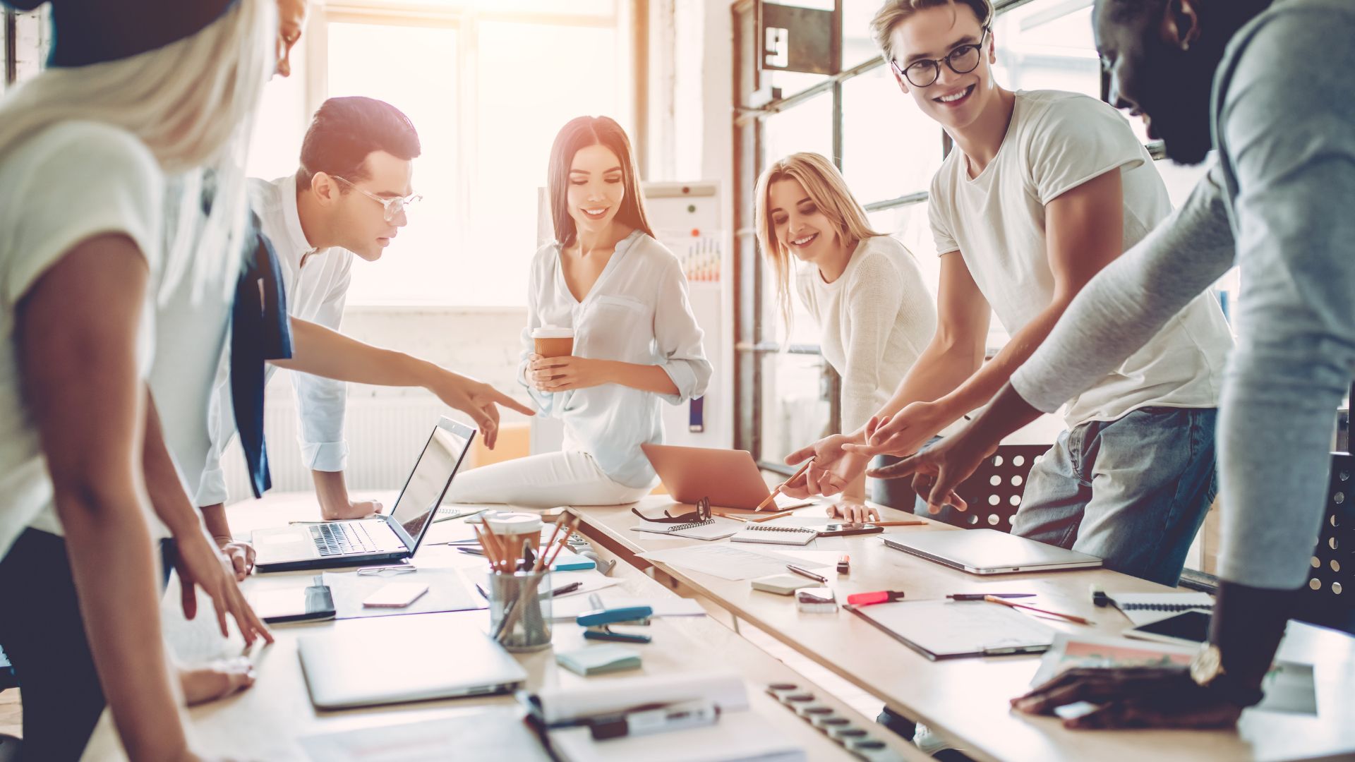 Generic stock photo of "business" happening by happy people standing around a conference room table pointing at things and doing business stuff
