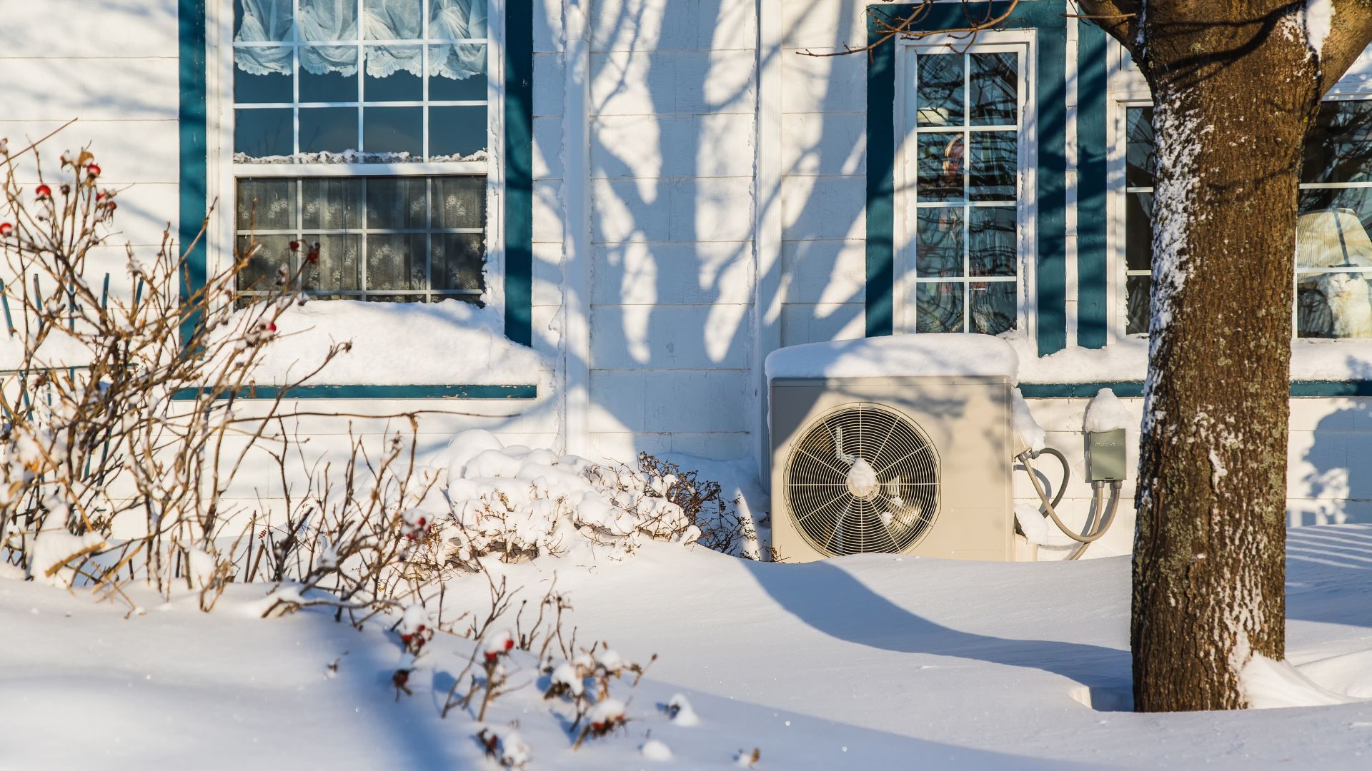 A heat pump outside of a house with several inches of snow on the ground