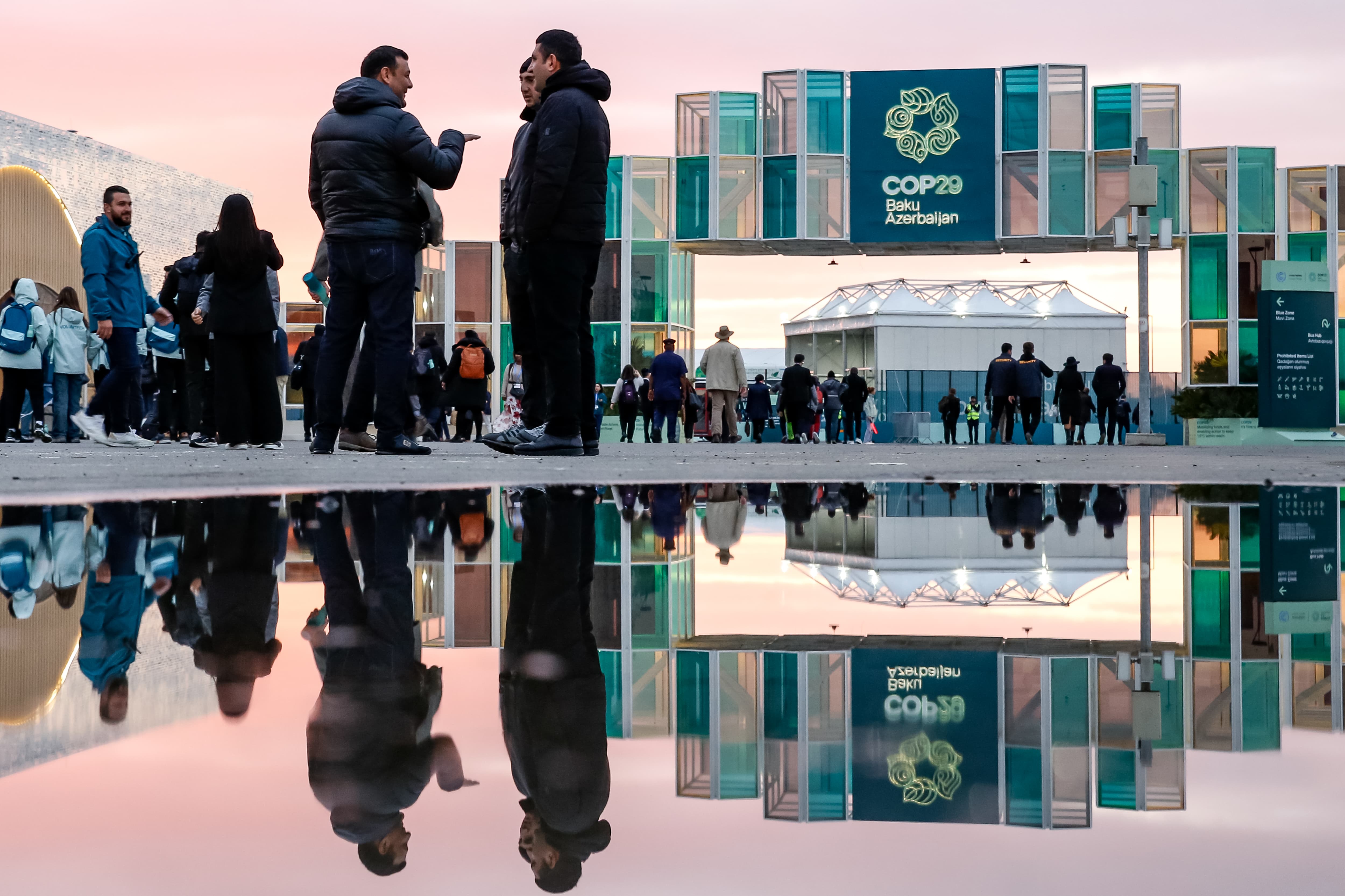 People chat outside a building displaying a teal COP29 banner.