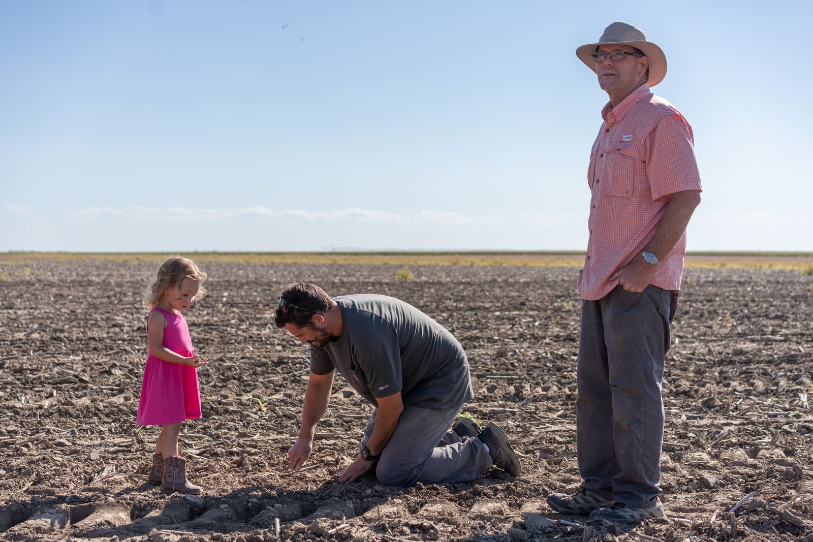 Dwane Roth standing next to his nephew Zion as he digs in the soil. His young daughter stands next to him.