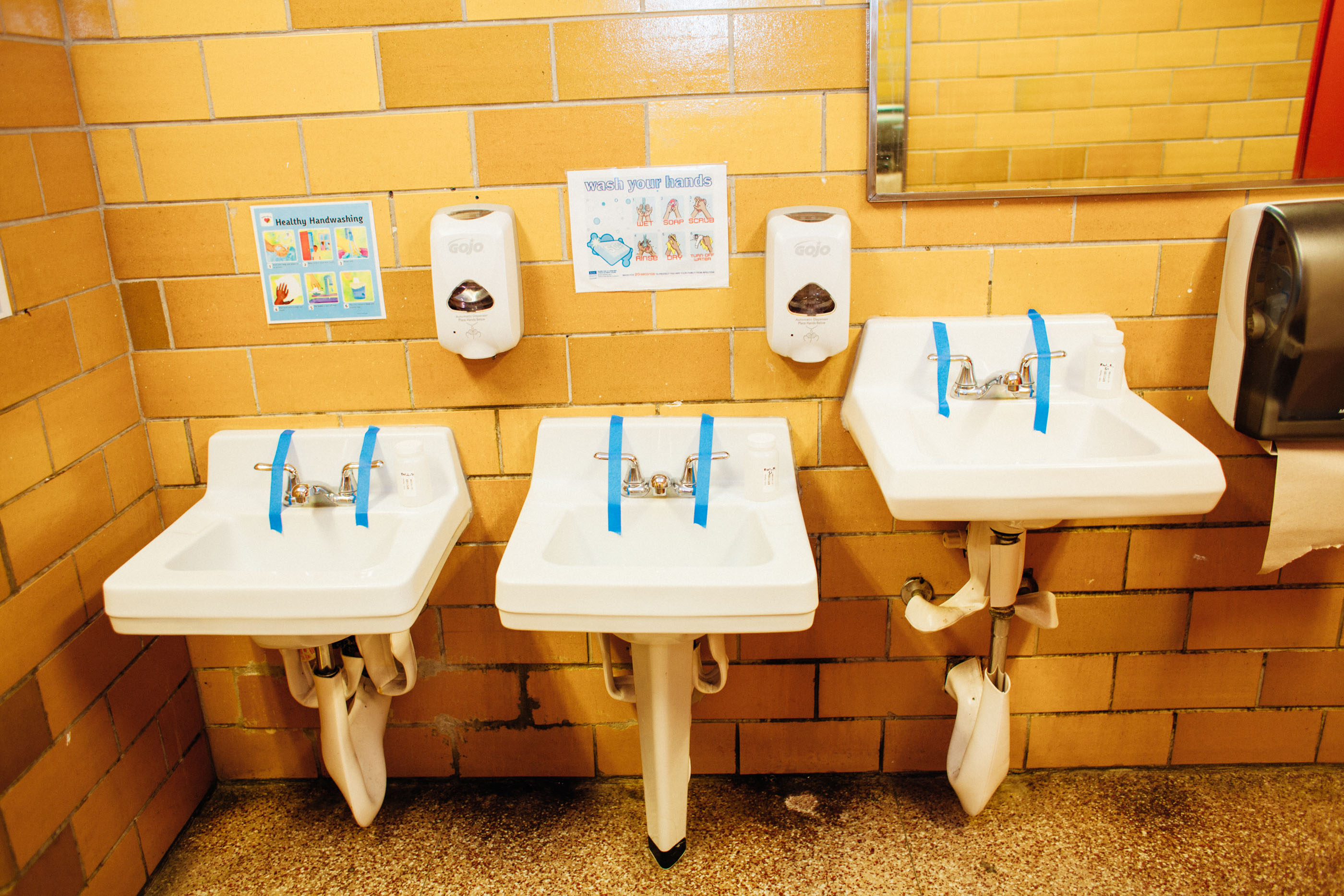 Three sinks in a restroom, with faucet handles taped off.