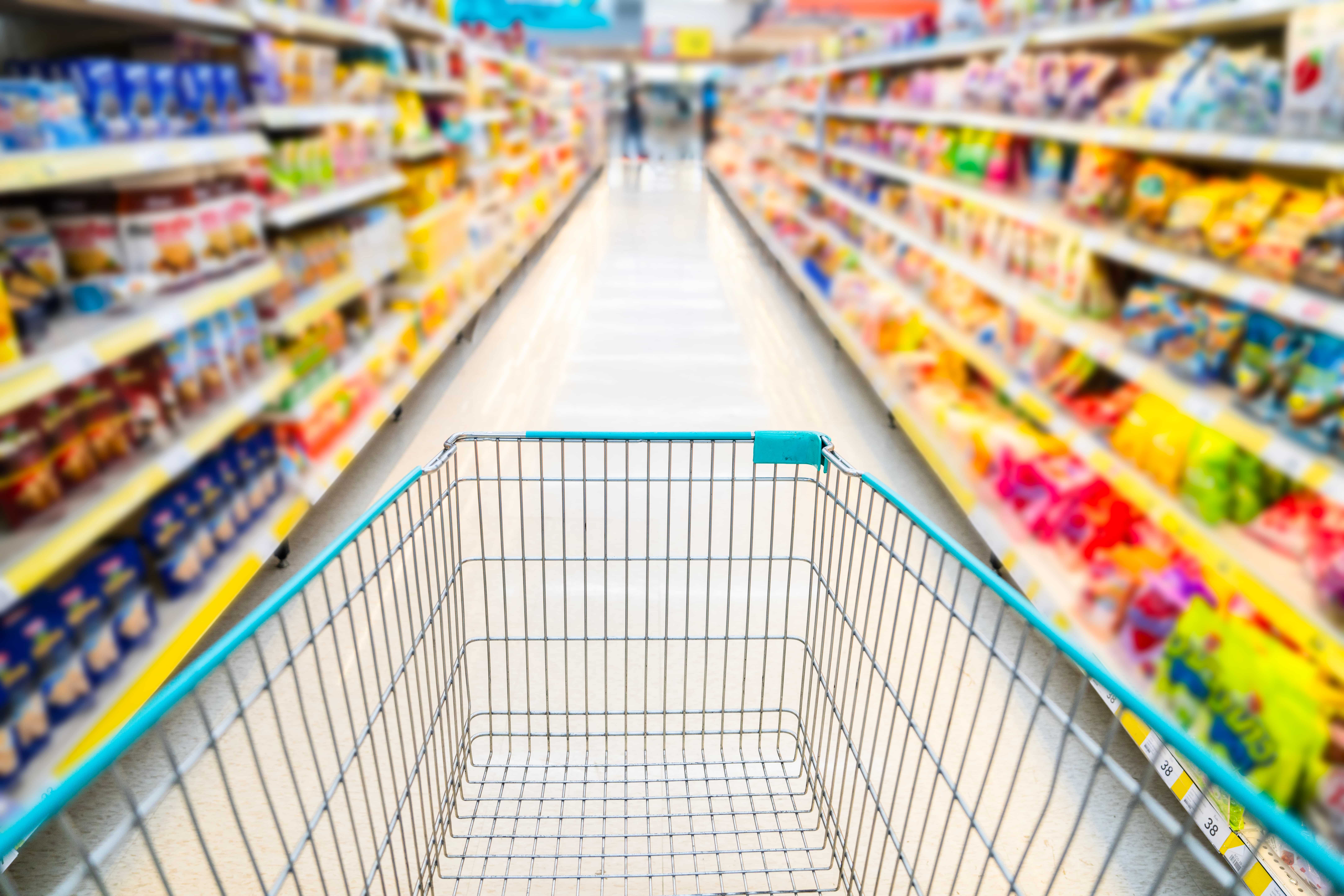 A shopping cart going down a colorful aisle at the grocery store.