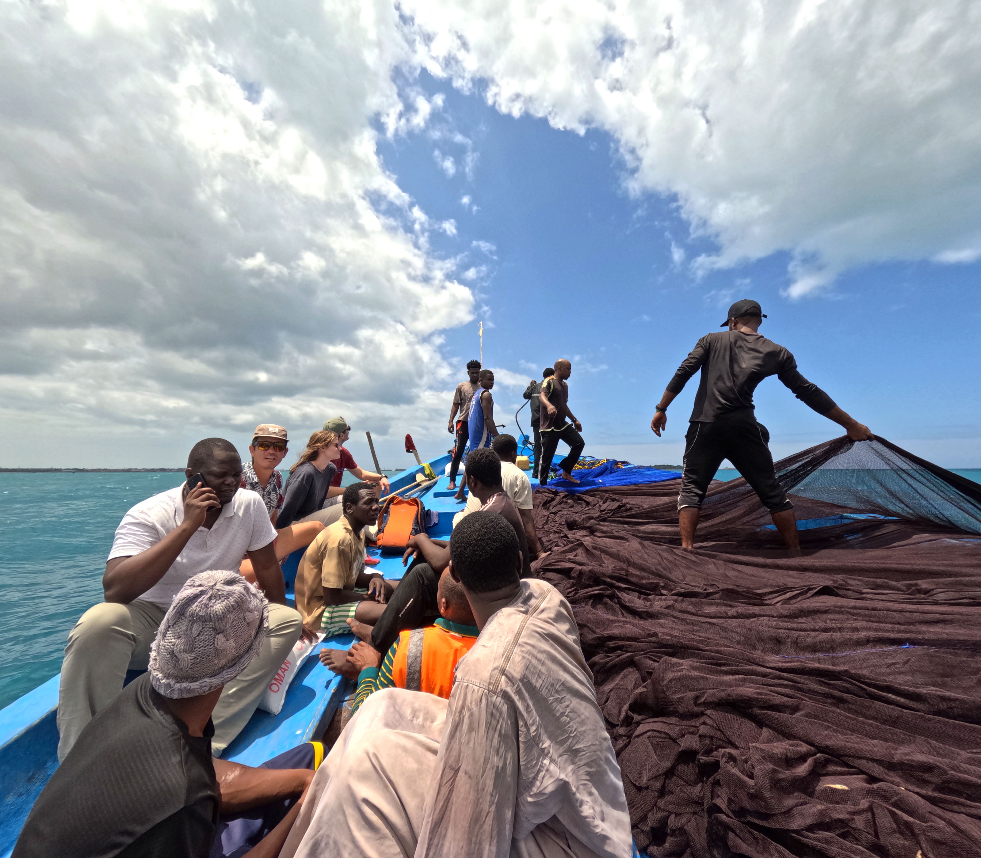 A large group of people sitting or at work on a small fishing boat.