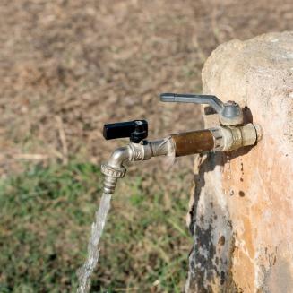 An outdoor water spigot with clear water flowing out of it