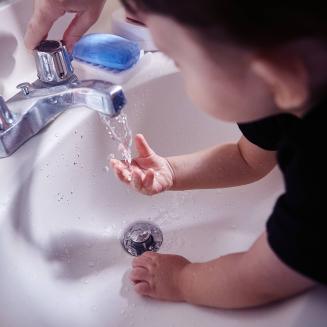 A young child washes his hands in a sink.