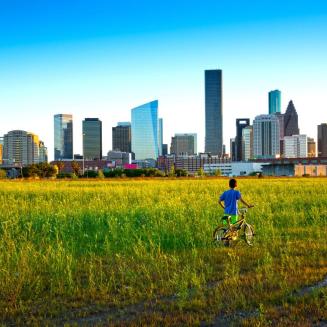 A young boy with his bicycle looks toward the imposing skyline of Houston