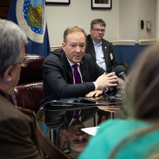EPA Administrator Lee Zeldin sits at a table speaking into a microphone to a group seated around the table