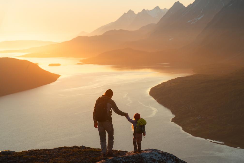 Dad and child on a mountain overlooking lake at sunset