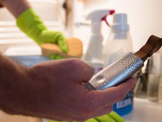 Person washing dishes and holding The Flow by Plume Labs, a personal air quality monitor that maps air pollution in real time.