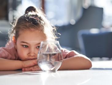 A small child looking at a glass of water.