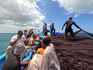 A large group of people sitting or at work on a small fishing boat.