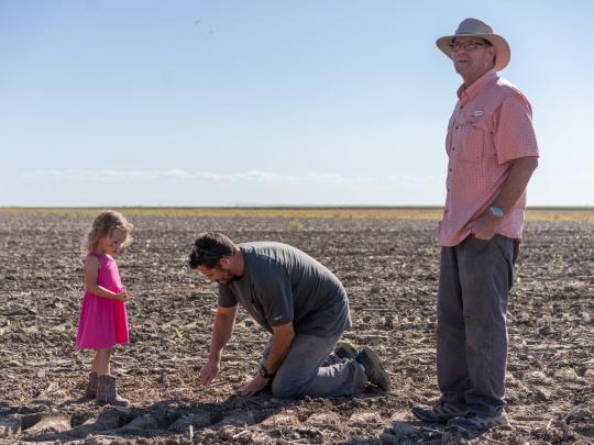 Dwane Roth standing next to his nephew Zion as he digs in the soil. His young daughter stands next to him.