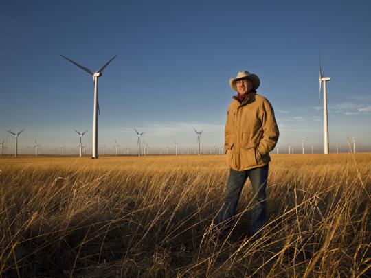 Pete Ferrell standing in a grassy field in front of wind turbines.